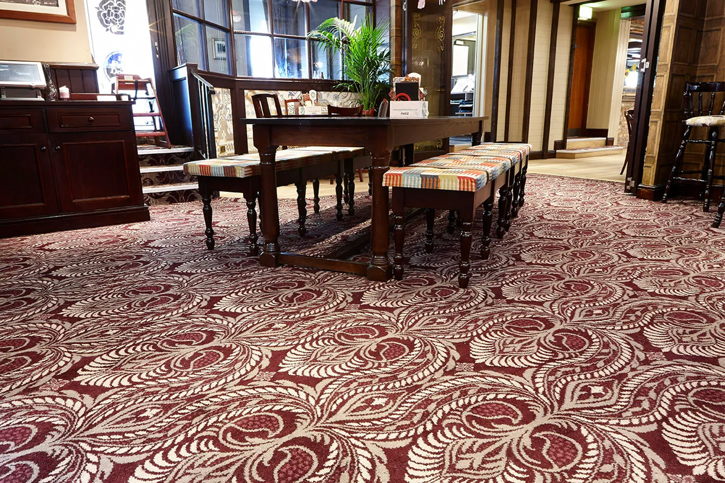 A dark red hotel carpet, designed by Wilton Carpets with white plant-like patterns
